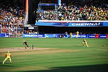 Cricketers in a game in front of nearly-full stands.